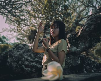 Young woman sitting on rock against trees