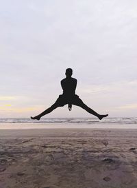 Silhouette man jumping at beach against sky during sunset