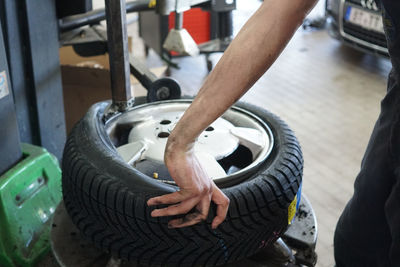 Midsection of mechanic holding tire on floor at auto repair shop