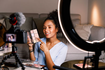 Smiling young woman showing beauty product while filming at home