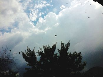 Low angle view of birds flying against cloudy sky