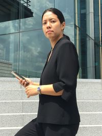 Portrait of businesswoman using mobile phone while moving up on steps