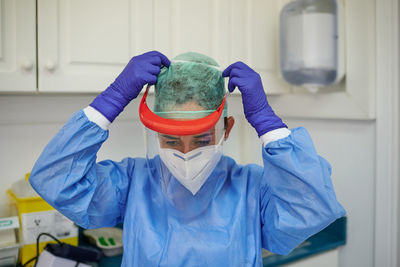 Unrecognizable female doctor in sterile uniform and gloves putting on protective shield in hospital while looking down