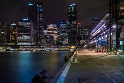 Illuminated buildings by river against sky in city at night