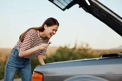 Side view of young woman sitting on car