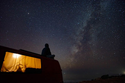 Woman sitting on motor home against sky at night