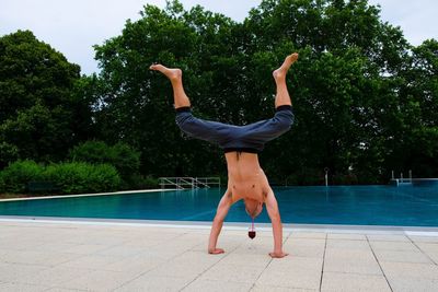 Shirtless man doing handstand against swimming pool