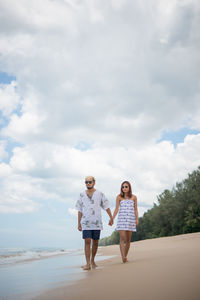 Man and woman walking at beach against sky