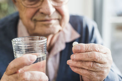 Hands of senior man holding tablet and glass of water, close up