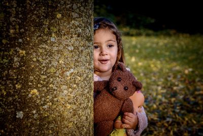 Portrait of cute girl holding toy against tree trunk