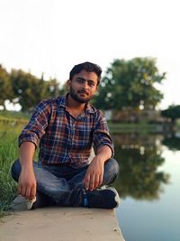 Portrait of young man sitting by lake