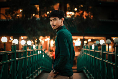 Portrait of young man standing against illuminated city at night