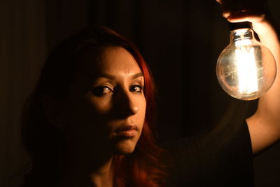 Close-up portrait of young woman holding light bulb