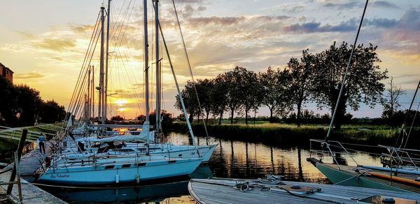 Boats moored in harbor at sunset