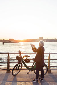 Full length of senior woman photographing while standing on promenade during sunset