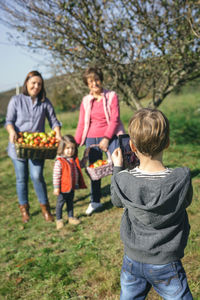 Rear view of boy photographing family from digital tablet on field