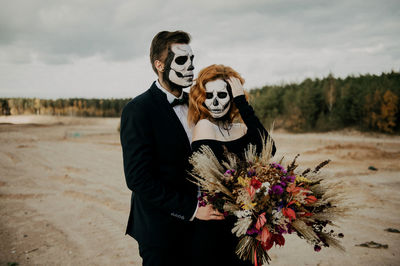 A couple in love celebrates halloween in costumes and makeup with a bouquet of dried flowers