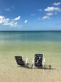 Empty chairs on beach against sky