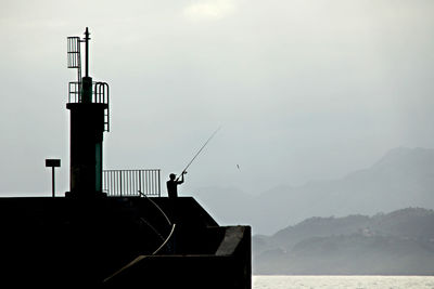 Silhouette building by sea against sky