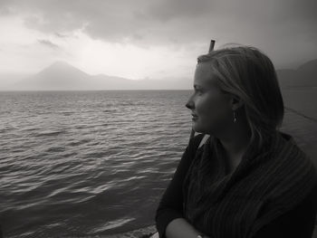 Thoughtful woman looking away while standing on shore against sky