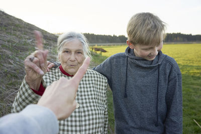 Cropped hand pointing against senior woman and teenage boy standing on grassy field