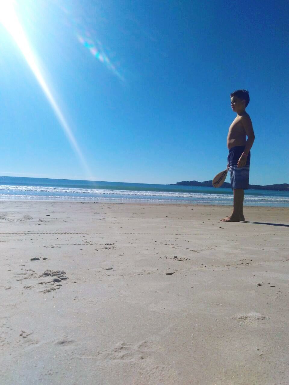 MAN STANDING ON BEACH AGAINST BLUE SKY