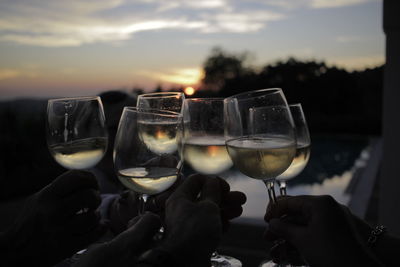 Close-up of hand holding wine glasses against sky during sunset