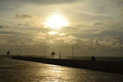 Silhouette man sitting on pier over sea against sky during sunset