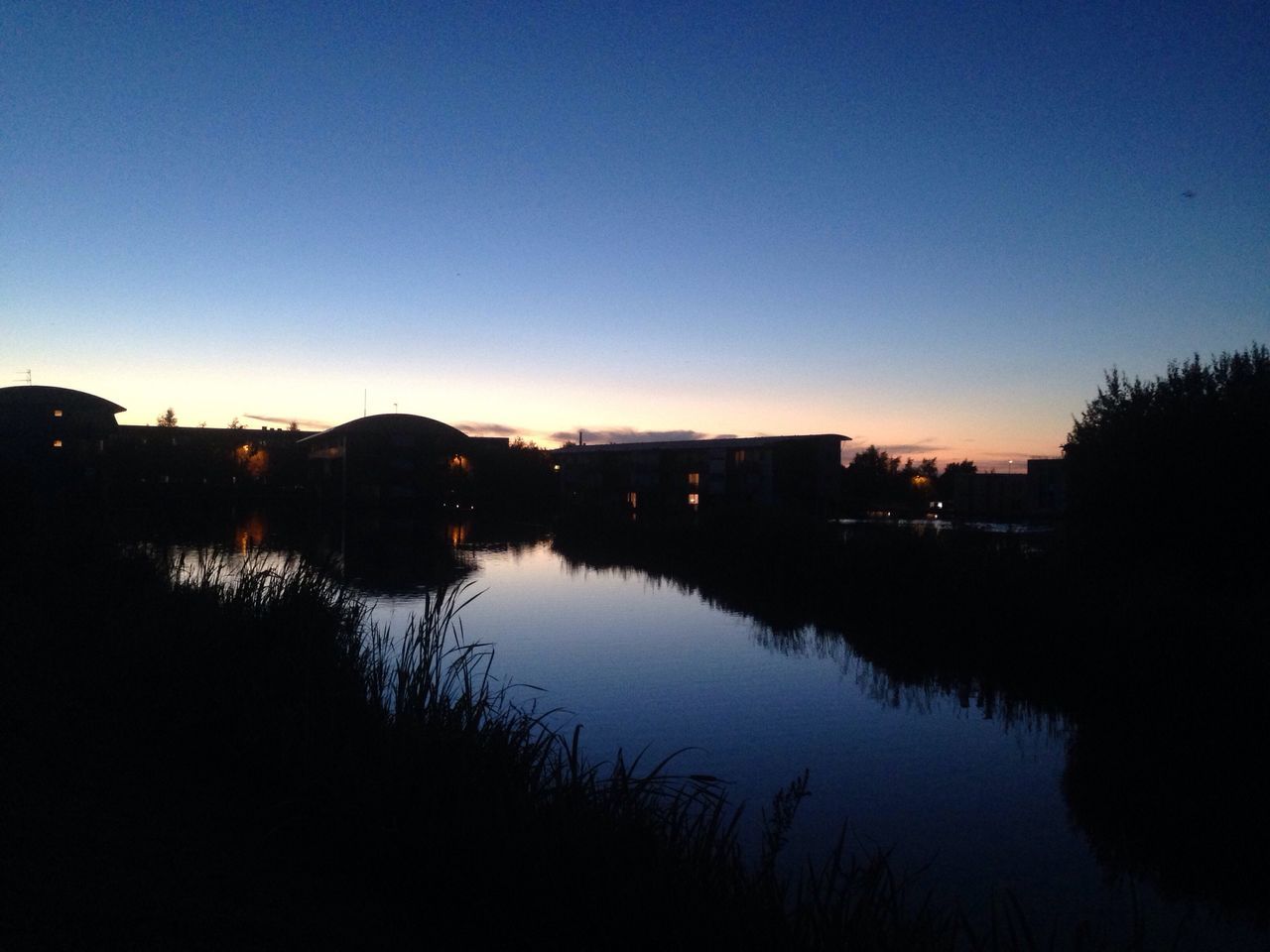 reflection, water, silhouette, lake, clear sky, copy space, calm, tranquility, tranquil scene, blue, mid distance, dark, outline, scenics, standing water, nature, beauty in nature, outdoors, countryside, solitude, lakeside, no people, bridge, remote, town