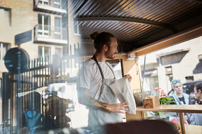 Young male owner packing food in paper bag at concession stand