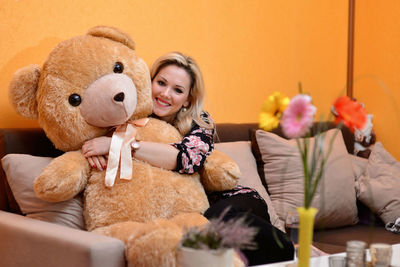 Portrait of smiling young woman with teddy bear sitting at home