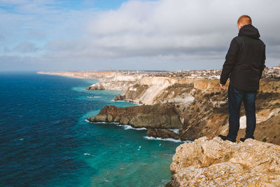 Rear view of man standing on rock by sea