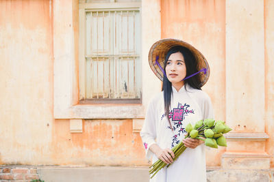 Portrait of young vietnamese woman standing against house