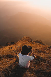 Rear view of man sitting on mountain against sky