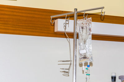 Saline drip hanging on metal hook against wall in hospital
