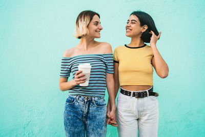 Happy young woman standing against blue wall