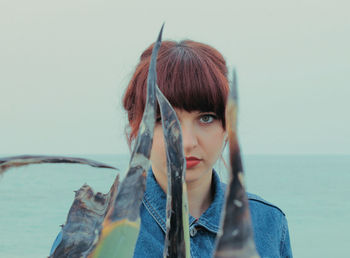 Portrait of woman looking through plants against sea