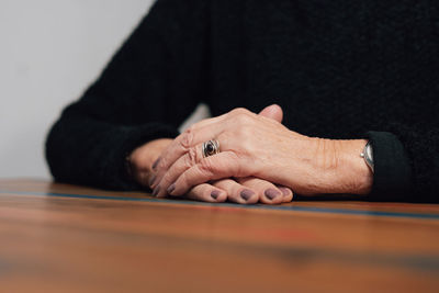 The pensioner has crossed her beautiful arms with wrinkles on her skin and is sitting at the table