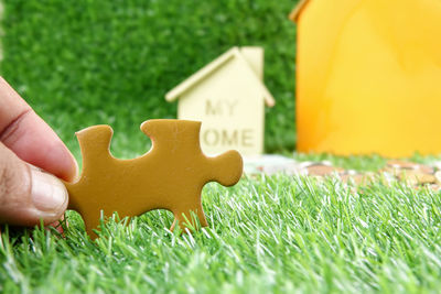 Cropped hand holding jigsaw piece against model house on field