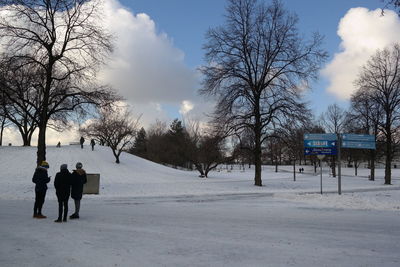 Rear view of people on snow covered field against sky