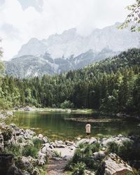 Rear view of woman looking at lake while standing against mountains