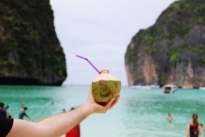 Cropped hand of man holding coconut at beach