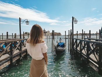 Woman standing on wooden post in canal against sky