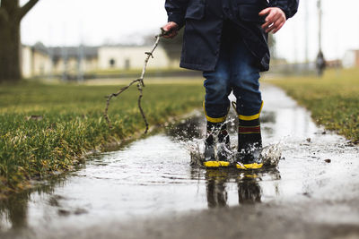 Low section of boy holding stick while jumping in puddle