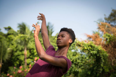 Low angle view of young man dancing against trees