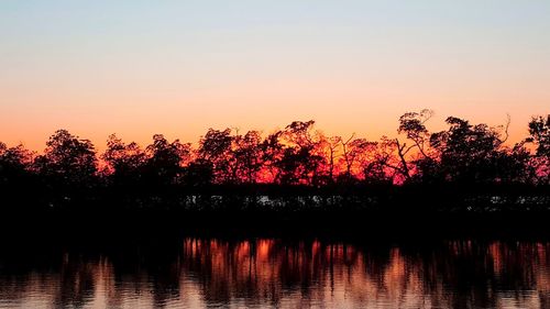 Silhouette trees by lake against sky at sunset
