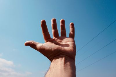 Low angle view of hand against blue sky