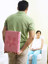 Rear view of man with gift standing against wife at home