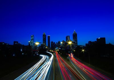 Light trails on road amidst buildings against blue sky