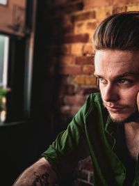 Close-up of thoughtful man sitting against brick wall